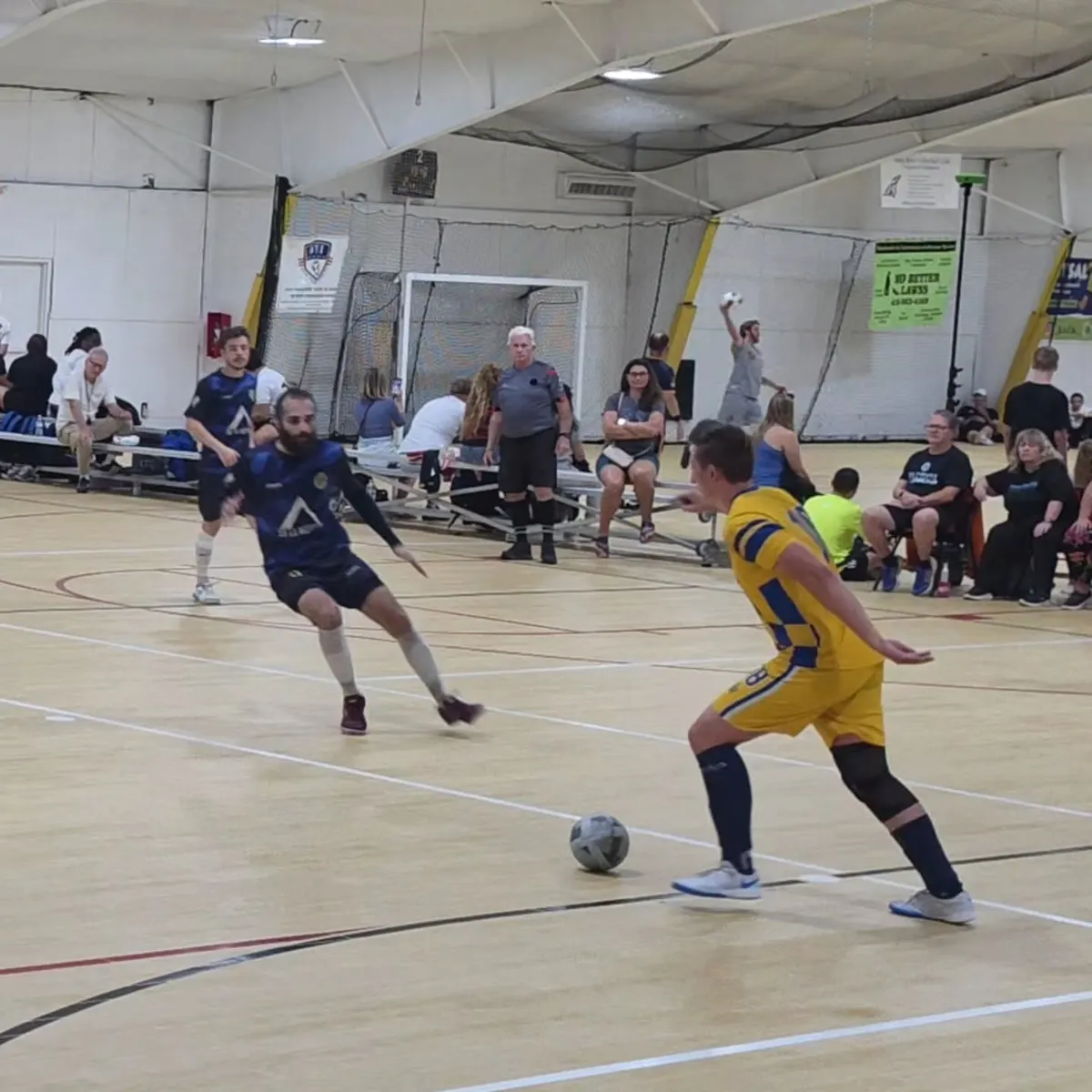Tyler in the Kings yellow kit taking on a defender in navy on a futsal court