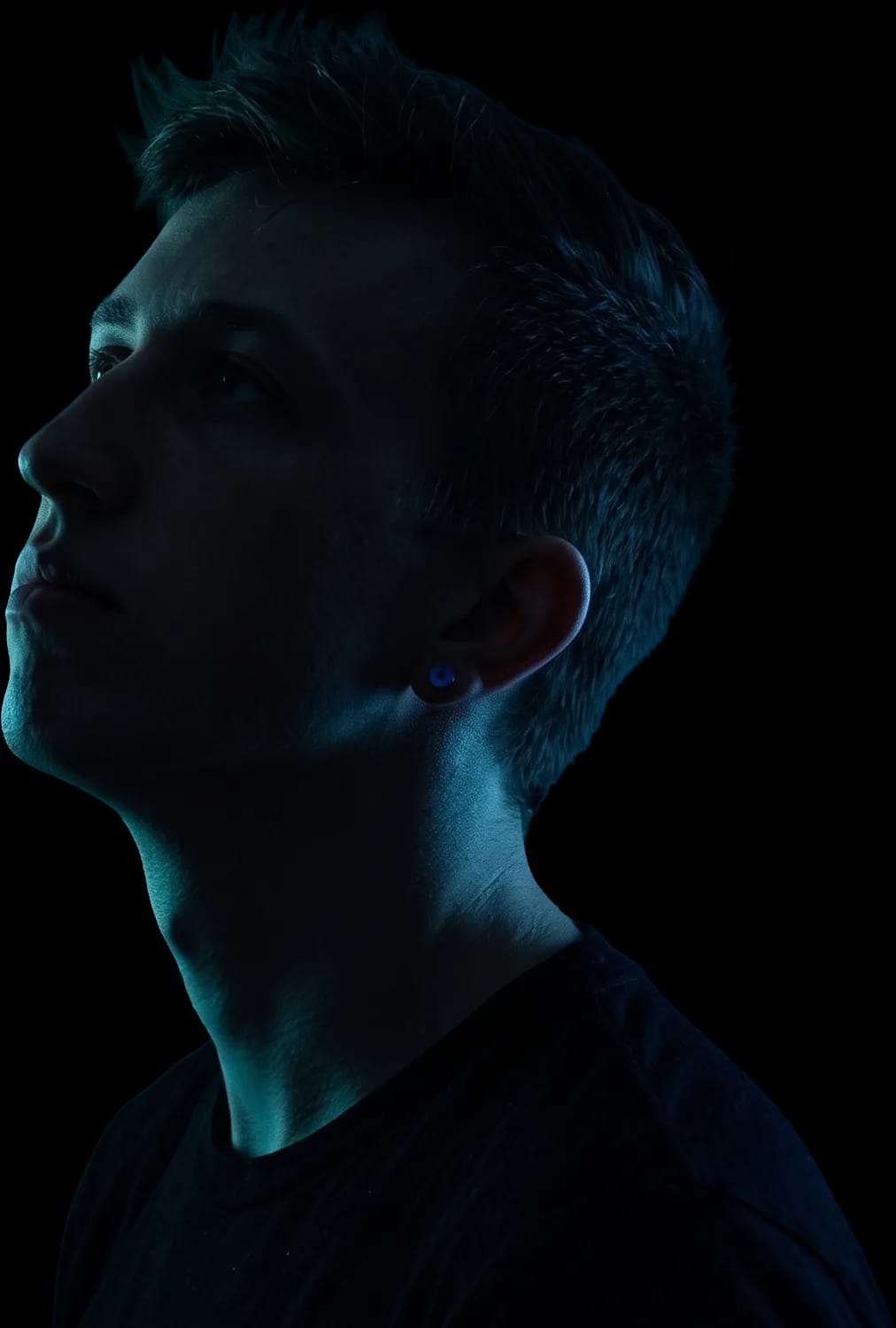 Tyler Jordan in profile, lit in teal, looking up and to the left